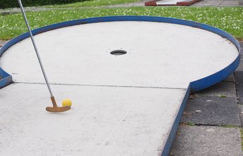 Ein Schläger schiebt einen Ball in ein Loch auf einer Minigolf-Anlage.