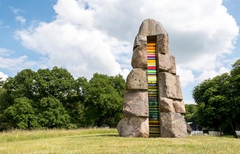 Bunte Steinskulptur auf einer grünen Wiese. 