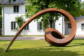 Kupferne Skulptur im Park der NordArt. Im Hintergrund ist ein weißes Gebäude.