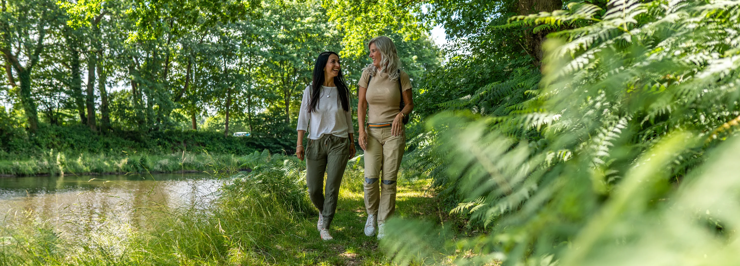 Zwei Frauen laufen entlang durch eine grüne Waldlandschaft entlang eines Sees.