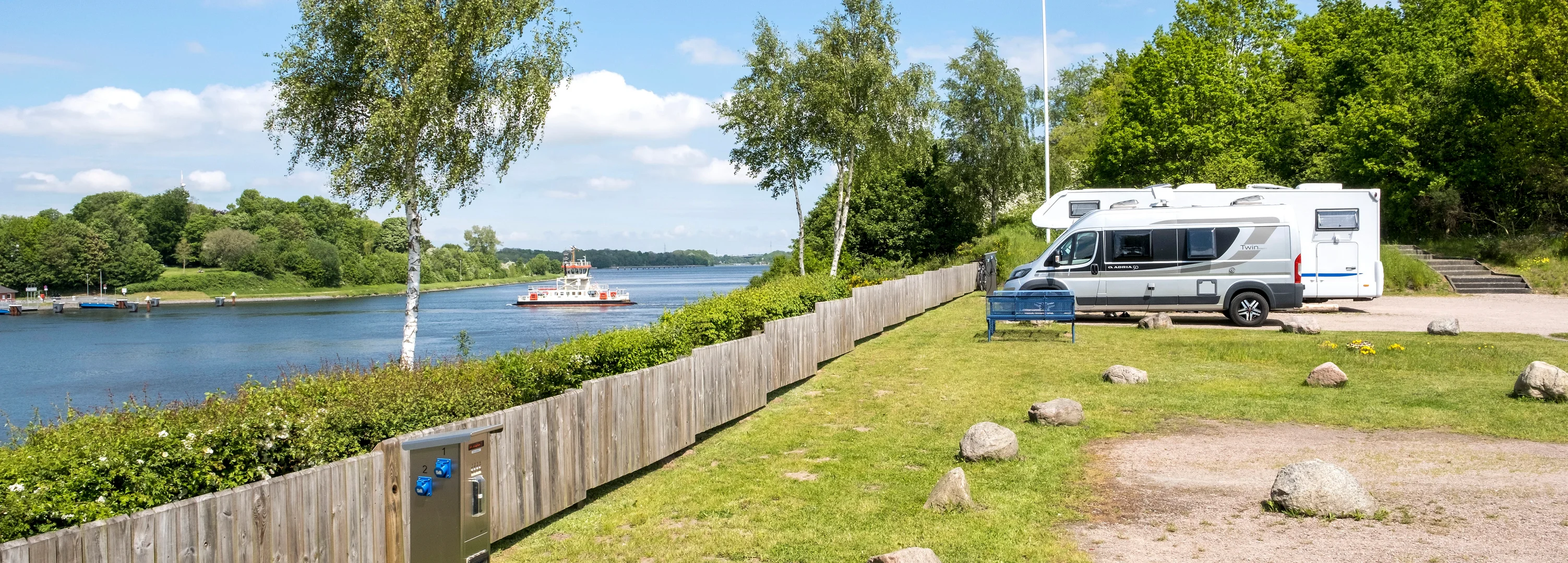 Ein Wohnmobil steht direkt am Nord-Ostsee-Kanal. Auf dem Wasser fährt eine Fähre.