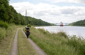 Bornholt am Nord-Ostsee-Kanal (© MHT.SH & Peter Lühr) Ein Radfahrer fährt am NOK entlang im Hintergrund sieht man ein Schiff auf dem NOK