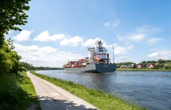 Schacht-Audorf_14 Ein großes Containerschiff fährt auf dem NOK entlang. Der Himmel ist blau.