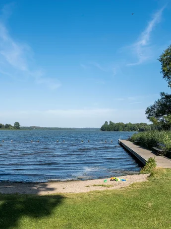 Badestelle mit Badesteg und grüner Liegewiese am Westensee im Sommer.