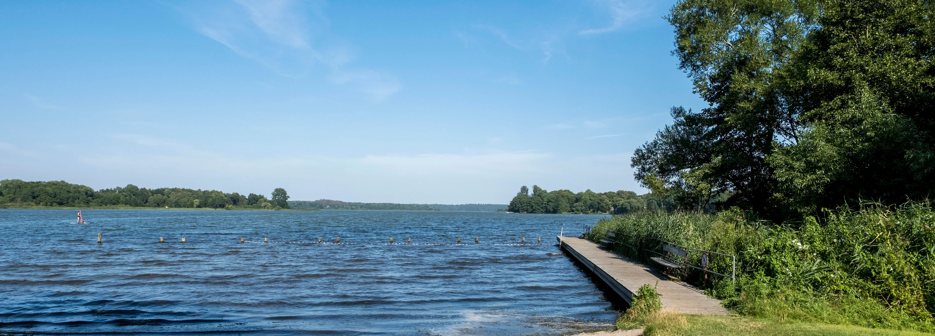 Badestelle mit Badesteg und grüner Liegewiese am Westensee im Sommer.