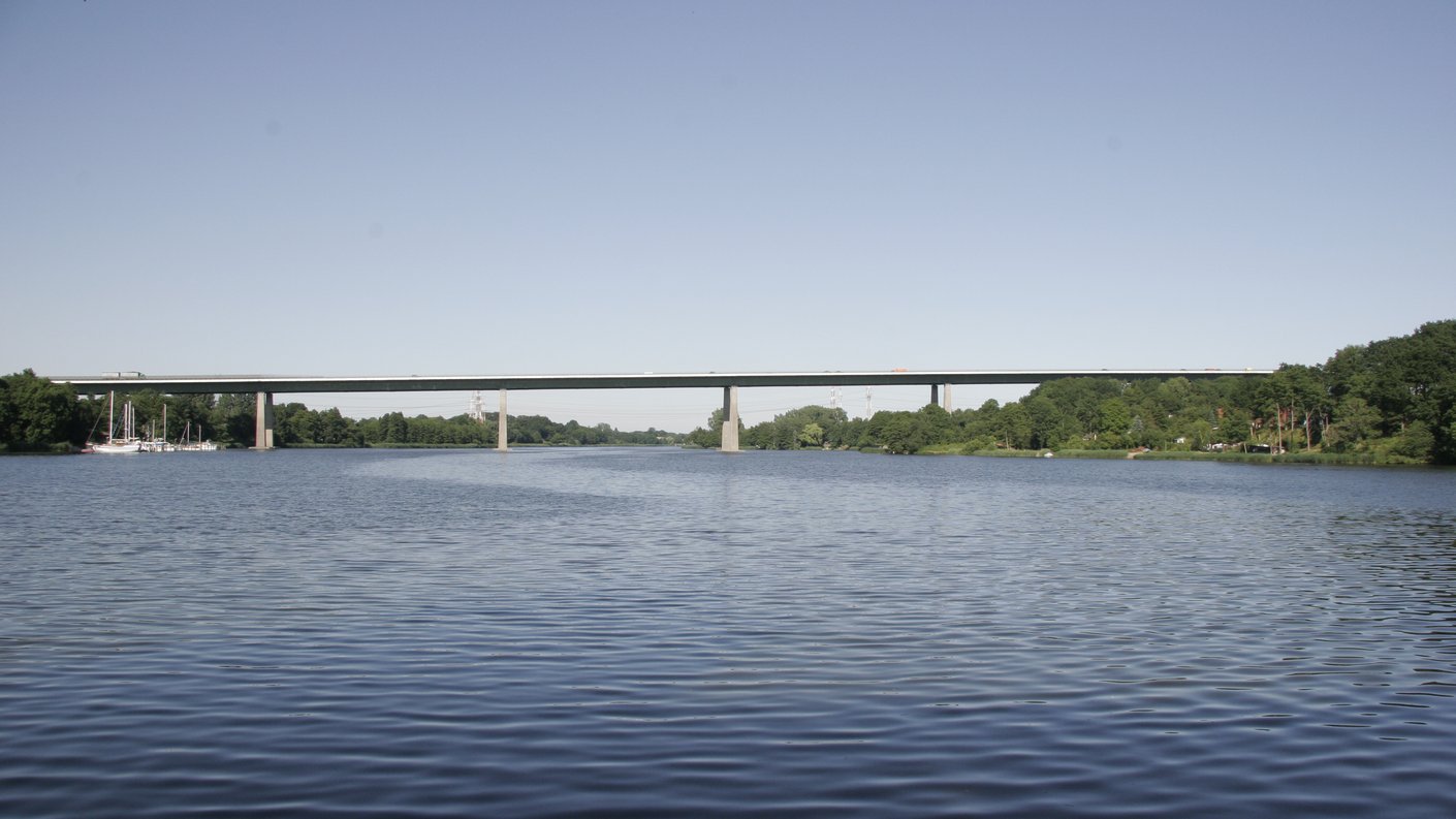Eine Brücke ist über einem Gewässer zu sehen. Der Himmel ist blau.