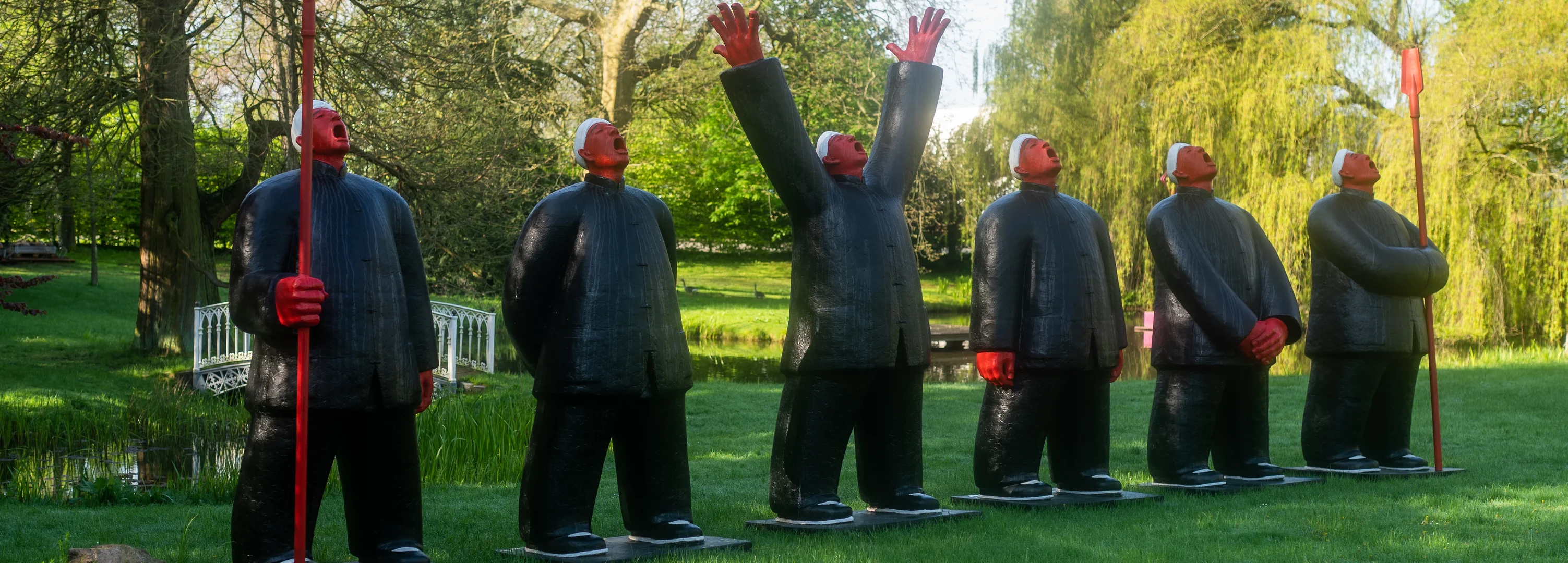 Menschliche Skulpturen in schwarz und rot stehen auf einer Wiese.