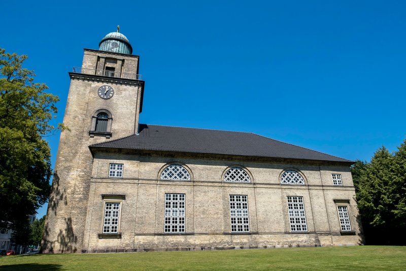 Die Vicelinkirche in Neumünster mit ihrem markanten Turm und großen Fenstern vor einem klaren blauen Himmel.