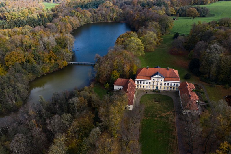 Luftaufnahme von Gut Emkendorf mit einem See und herbstlichen Bäumen.