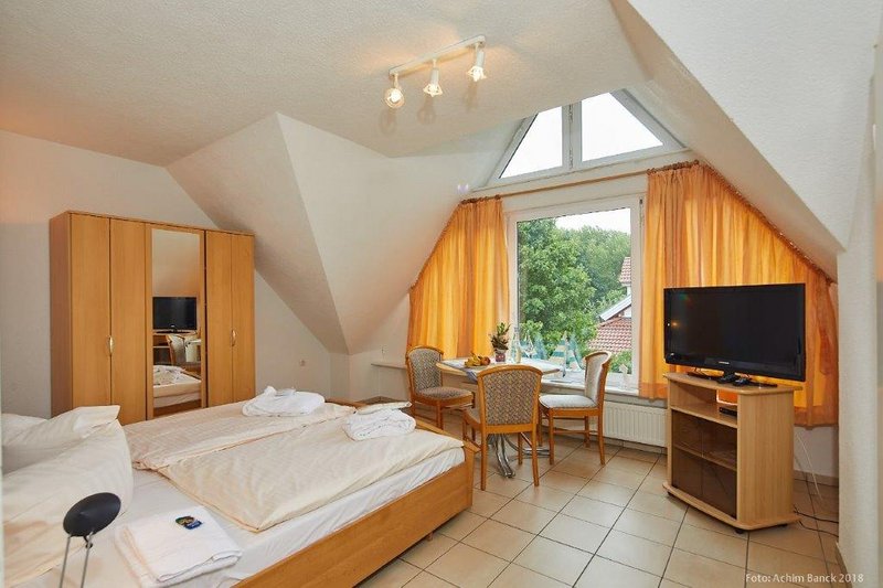 Hotelzimmer mit Doppelbett, Tisch und Stühlen vor einem großen Fenster mit Vorhängen.