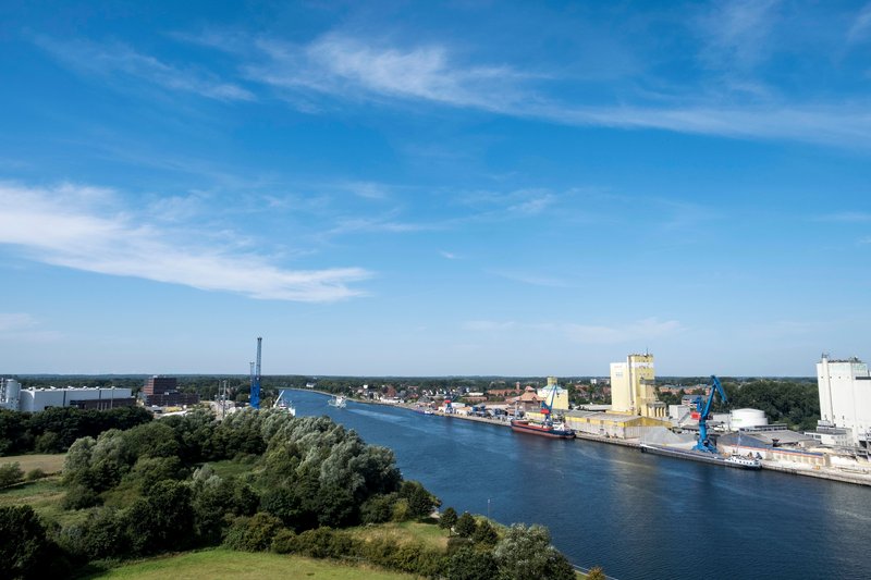 Blick auf den Nord-Ostsee-Kanal mit blauen Himmel und Industrieanlagen am Ufer.