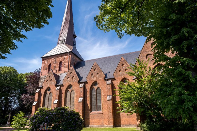 Sankt Martin Kirche in Nortorf, umgeben von Bäumen und blauem Himmel.