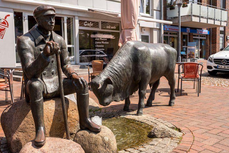 Bronzestatue eines sitzenden Mannes mit Stock neben einem Stier in Hohenwestedt.