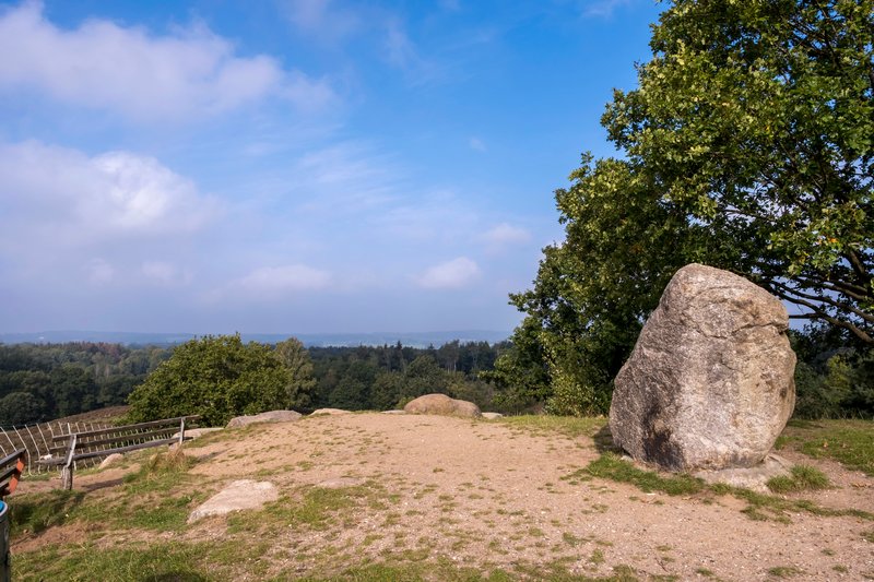 Aussichtspunkt mit großem Felsen und Blick auf bewaldete Landschaft.