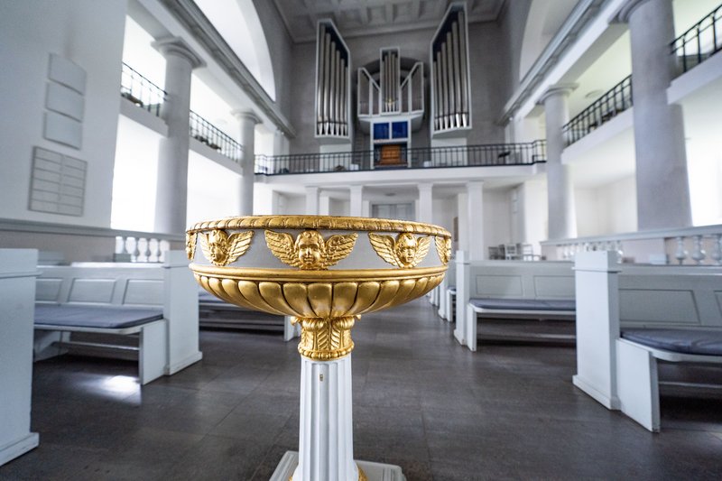 Ein kunstvoll verziertes Taufbecken in einer Kirche mit Orgel im Hintergrund.