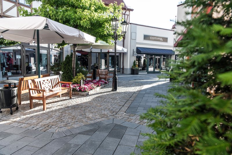 Ein ruhiger Bereich im Neumünster Outlet-Center mit Bänken, Blumenbeeten und Geschäften im Hintergrund.