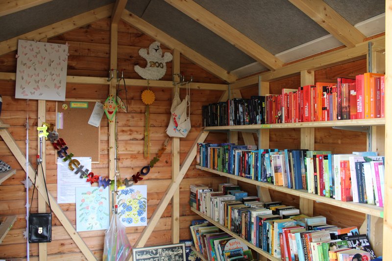 Innenansicht einer Tauschhütte mit Bücherregalen und Dekorationen an den Wänden.