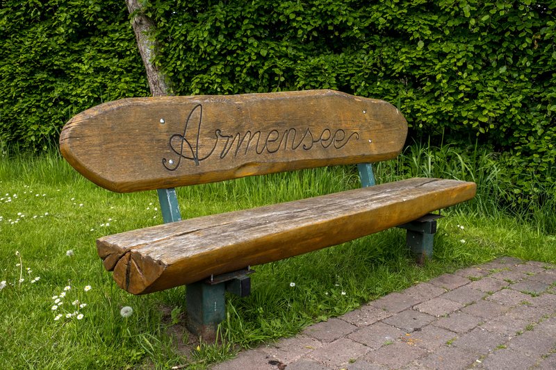 Holzbank mit der Aufschrift 'Armensee' vor einer Hecke.