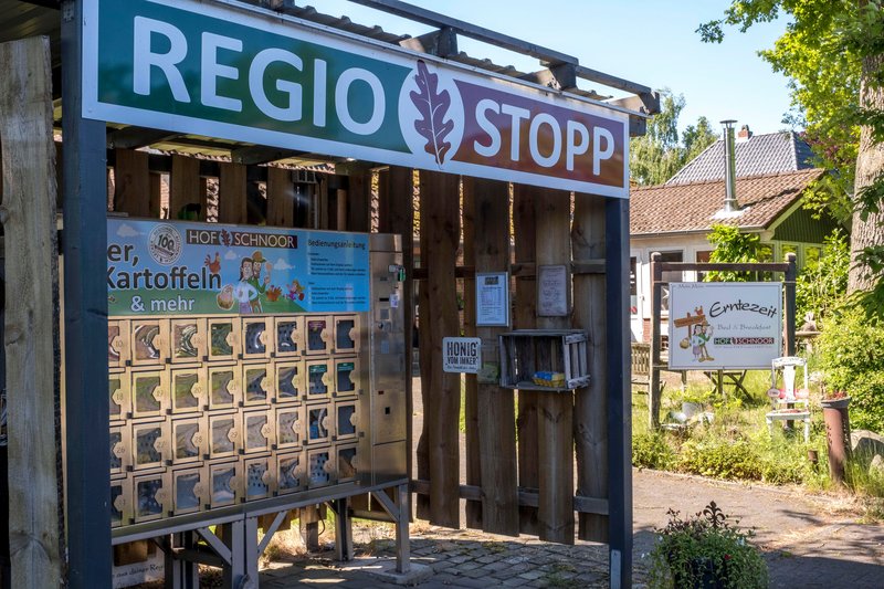Ein Verkaufsautomat auf dem Hof Schnoor mit regionalen Produkten wie Kartoffeln. Im Hintergrund ein Schild mit der Aufschrift 'Erntezeit Bed & Breakfast'.