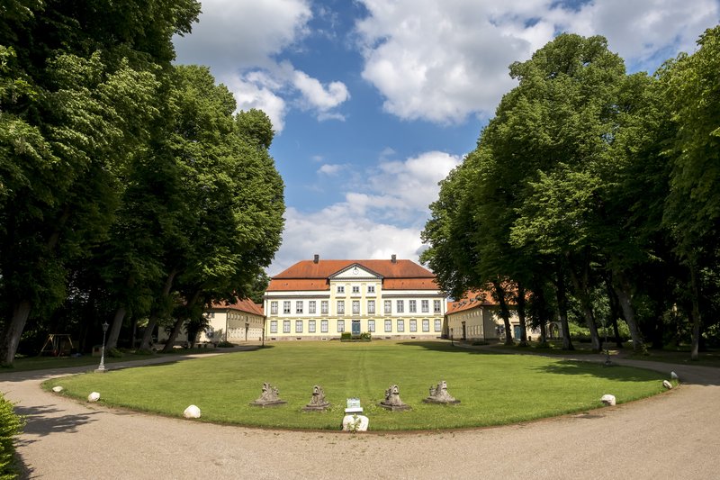 Herrenhaus Gut Emkendorf mit symmetrischem Garten und Bäumen.