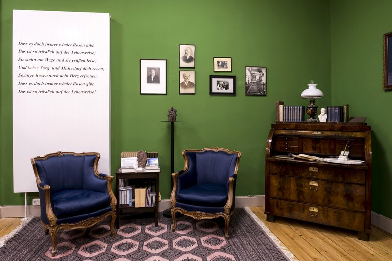 Ein Raum im Heimatmuseum Hanerau-Hademarschen mit grüner Wand, antiken Möbeln und historischen Fotos.