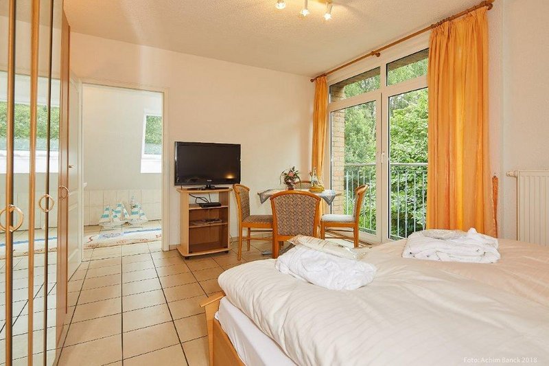 Hotelzimmer mit Doppelbett, Fernseher, Tisch und Stühlen, Balkon mit Blick ins Grüne.