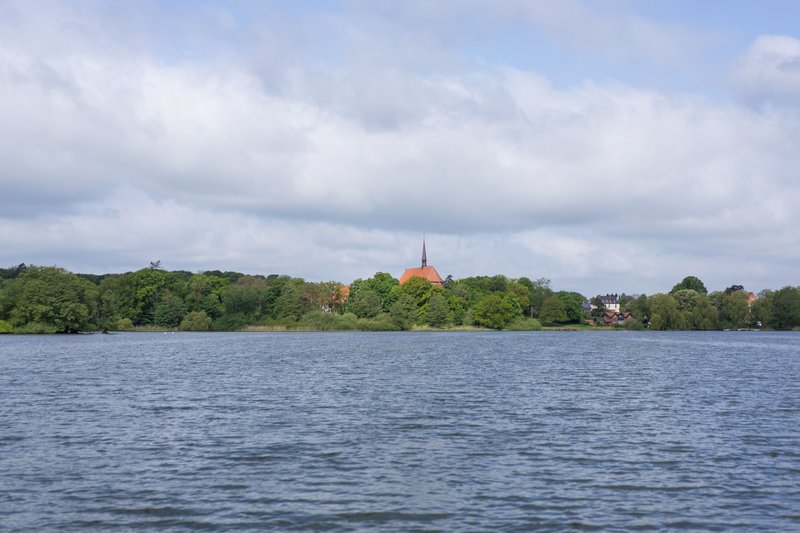 Blick über den Bordesholmer See auf die Klosterkirche, umgeben von Bäumen und Häusern.