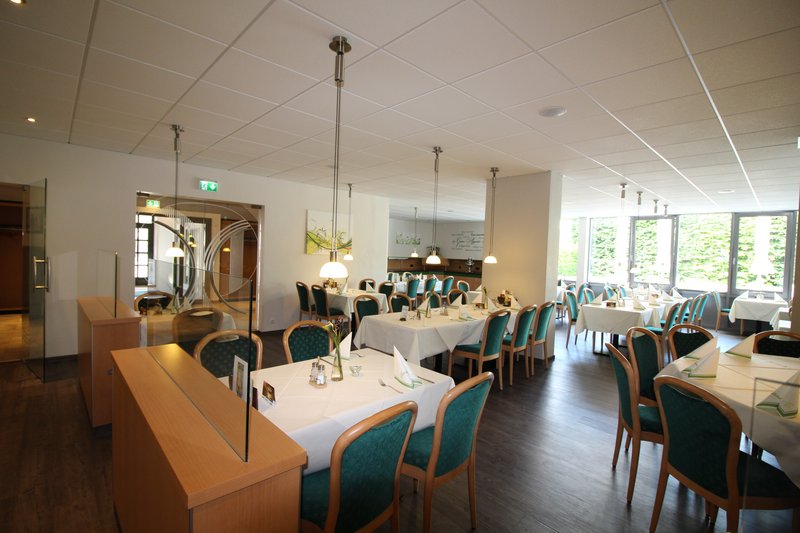 Innenansicht eines Hotelrestaurants mit gedeckten Tischen und grünen Stühlen.