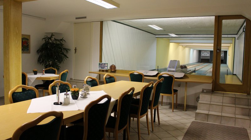Ein Hotelraum mit Tischen und Stühlen, neben einer Kegelbahn hinter einer Glaswand.
