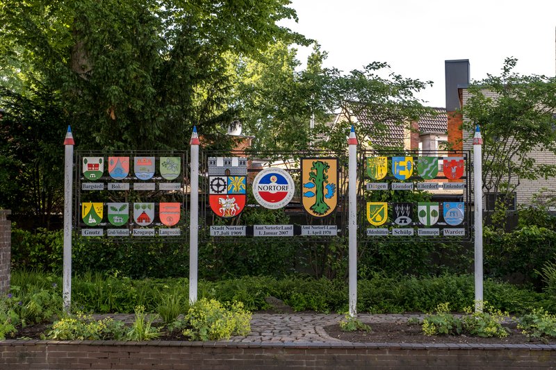 Schilder mit Wappen der Gemeinden des Amts Nortorfer Land in einem Garten.