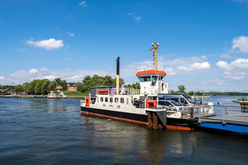 Eine Fähre transportiert Autos über einen Fluss bei sonnigem Wetter.