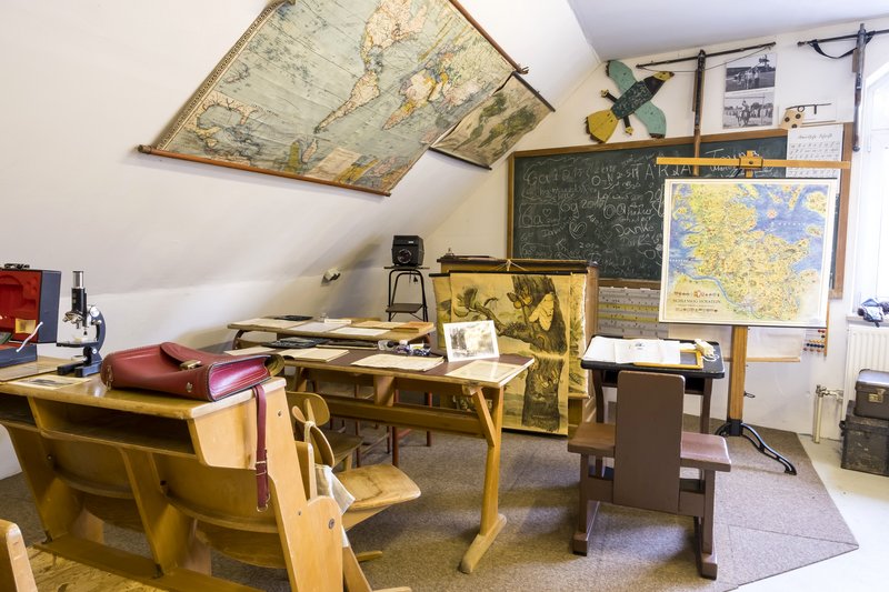 Ein Klassenzimmer im Retro-Stil mit alten Karten, einer Tafel und Schulbänken.