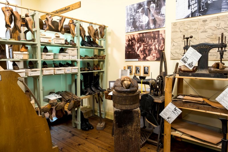 Innenansicht eines Schuhmacherraums im Heimatmuseum Hanerau-Hademarschen mit Schuhen, Werkzeugen und historischen Fotos.