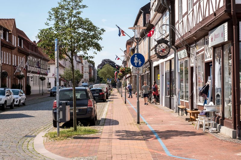 Straßenszene in Rendsburg mit blauer Linie auf dem Gehweg und Fachwerkhäusern.
