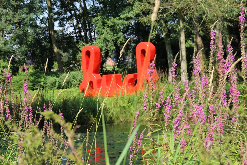 Roter Schriftzug im Gerisch-Park hinter lila Blumen und Gräsern.