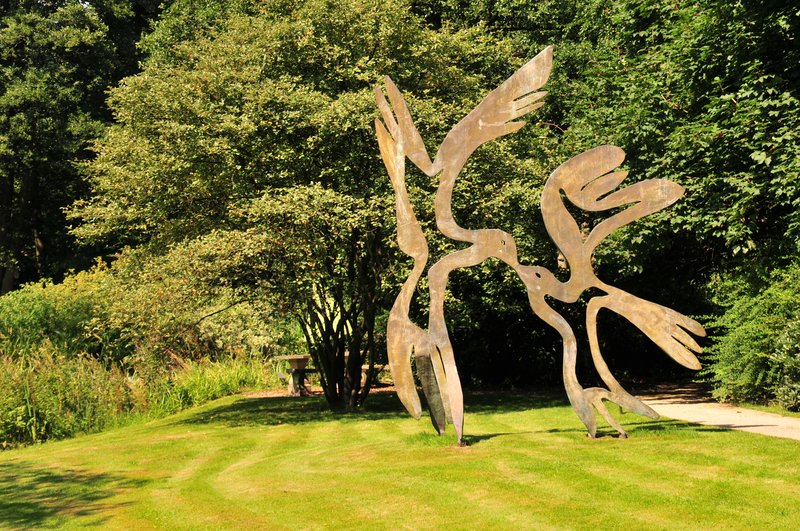 Metallskulptur von zwei stilisierten Vögeln in einem Park.