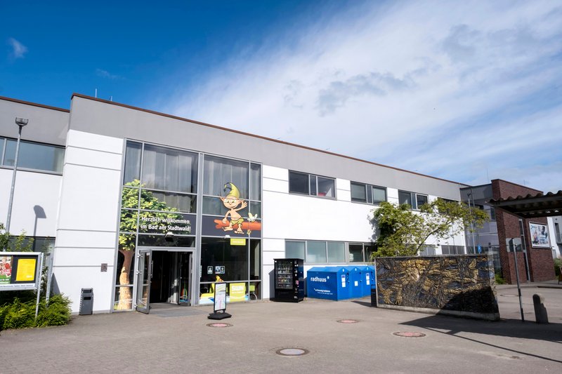 Eingang des Gebäudes 'Bad am Stadtwald' mit Glasfront und Cartoon-Figur.