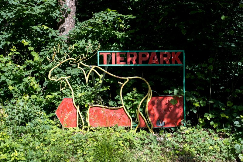 Ein Schild mit der Aufschrift 'Tierpark' und einem Hirschmotiv im Wald.