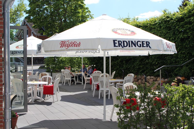 Außenterrasse eines Cafés mit weißen Plastikstühlen und Tischen unter großen Erdinger Sonnenschirmen.