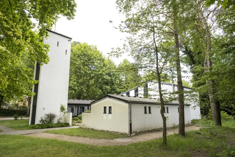 Weiße Kirche mit Turm, umgeben von Bäumen und Grünflächen.