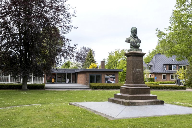 Büste von M. H. Holler vor dem Eisenkunstgussmuseum in einem grünen Park.