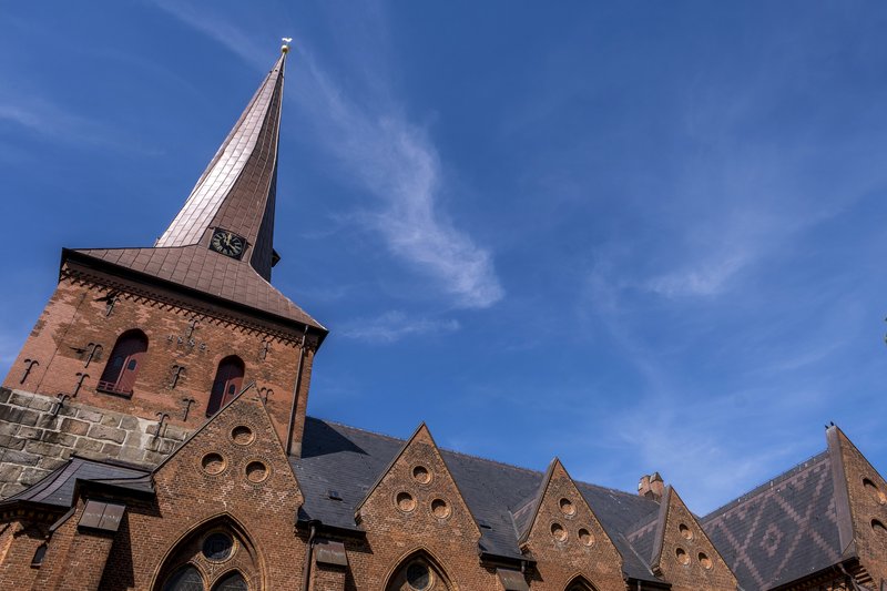 Sankt Martin Kirche in Nortorf mit rotem Backstein und spitzem Turm vor blauem Himmel.