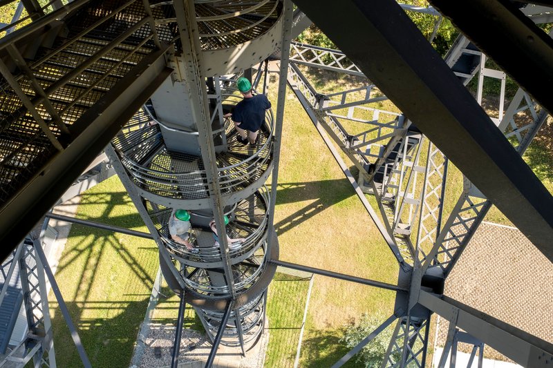 Menschen mit grünen Helmen steigen eine Wendeltreppe auf der Eisenbahnhochbrücke Rendsburg hinauf.