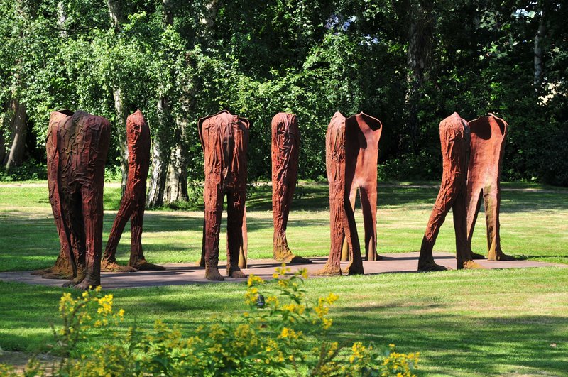Skulpturen von kopflosen Figuren in einem Park mit Bäumen im Hintergrund.