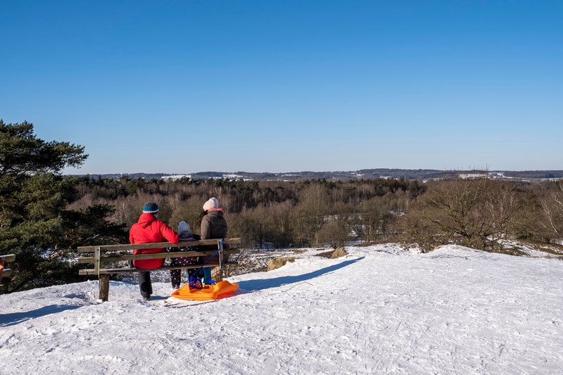 Eine Familie sitzt auf einer Bank und blickt über eine verschneite Landschaft.
